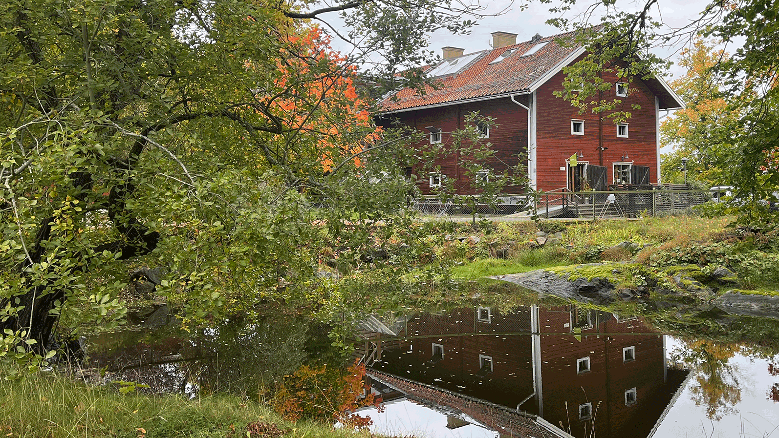 Skäve magasin i höstskrud, speglar sig i vattnet.