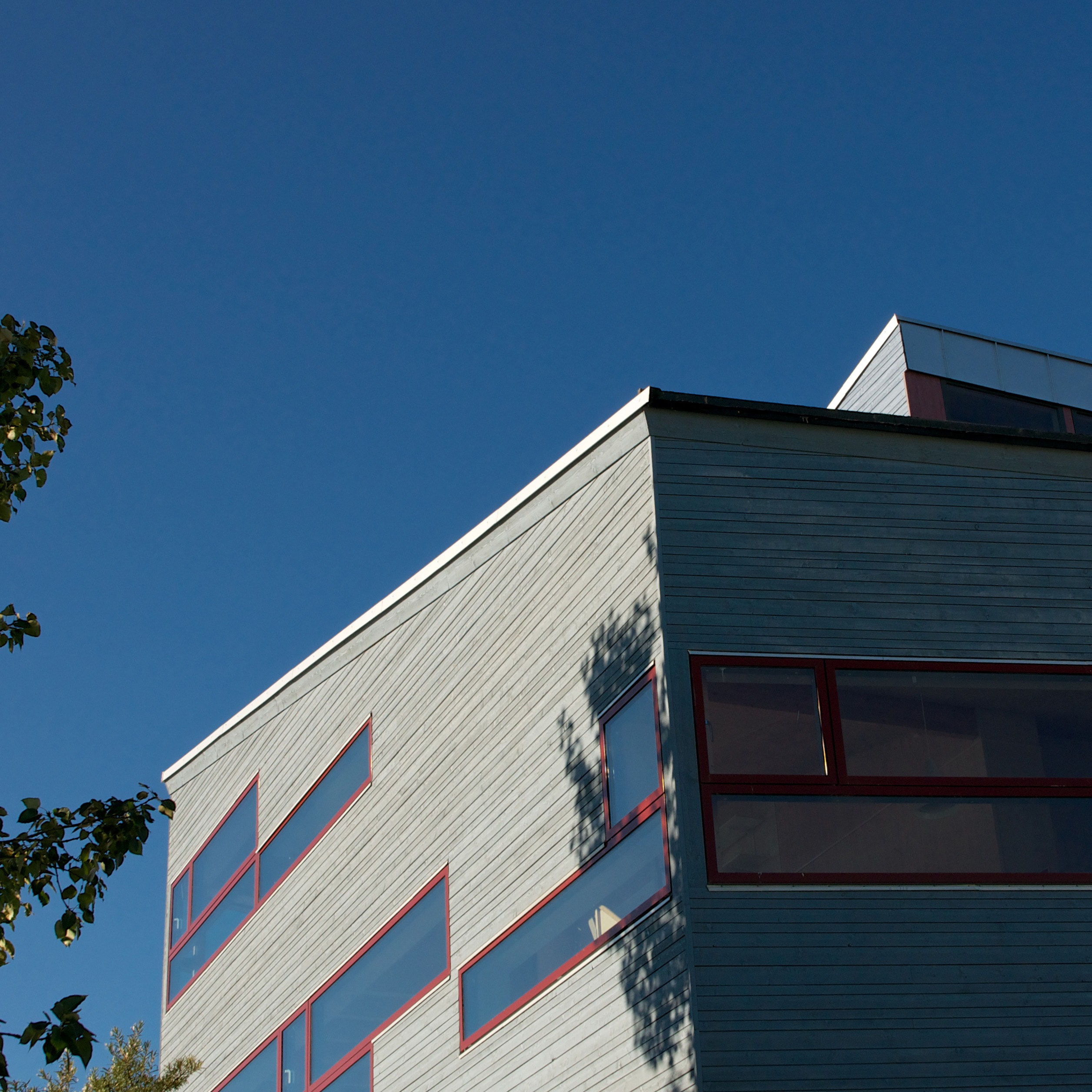 Grått hus som skuggas delvis av ett träd. Klarblå himmel. 