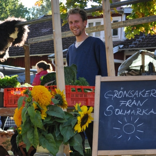 Person står och trängs bland annat bland blommor och en skylt.