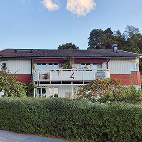 Ett parhus med svart tak och utanför en grön häck.