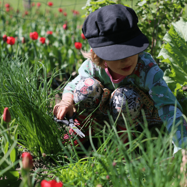 Barnet sitter på ängen skyddas av solen med långärmat och en keps.