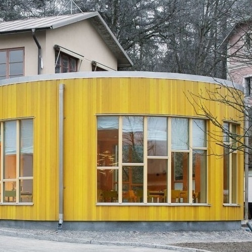 En gul rundad träbyggnad där träden saknar blad och det är mer grått ute.